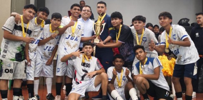 Un grupo de estudiantes celebra su victoria en los Juegos Intercolegiados 2025 de Puente Aranda. Los jóvenes, vestidos con uniformes deportivos y medallas doradas en el cuello, posan sonrientes alrededor de un gran trofeo dorado que sostienen junto a dos adultos. La escena refleja alegría, unión y logro colectivo al finalizar la competencia deportiva.