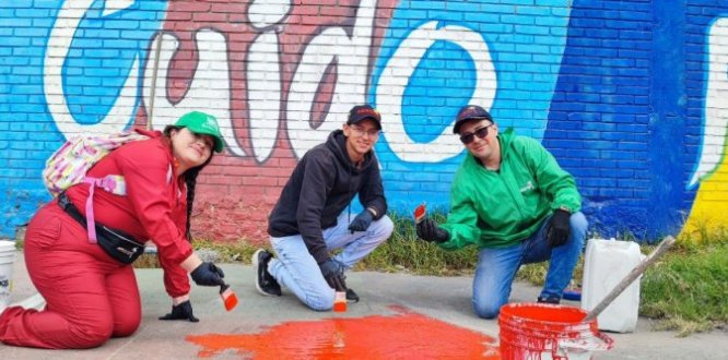 La estrategia “1000 en 1 Día” llega a Puente Aranda con actividades de transformación colectiva “Tres personas pintan el piso de color rojo frente a un mural colorido con la palabra ‘Cuido’, como parte de una jornada comunitaria de embellecimiento en Puente Aranda.”