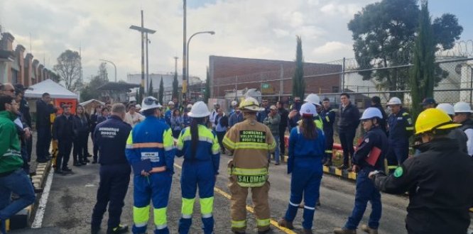 Funcionarios y equipos de emergencia participan en el Simulacro Distrital 2025 en Puente Aranda. En la imagen, se observa a personal de Bomberos Bogotá, brigadistas industriales y trabajadores con cascos y uniformes de seguridad recibiendo instrucciones en una zona industrial. El ejercicio demuestra la organización y el compromiso de la localidad con la prevención y la gestión del riesgo.