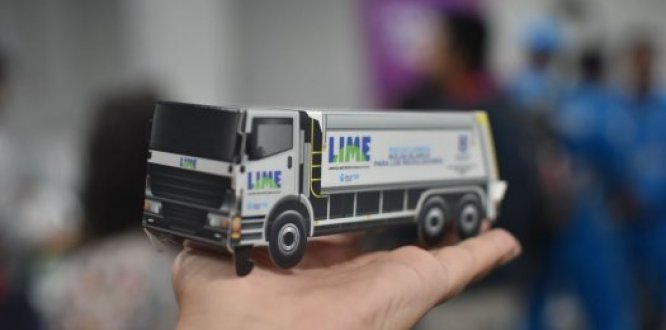 Segundo Foro Ambiental de Puente Aranda: un espacio de encuentro y reflexión "Persona sostiene en la mano una maqueta en miniatura de un camión de recolección de basura de la empresa LIME, con fondo desenfocado de personas."