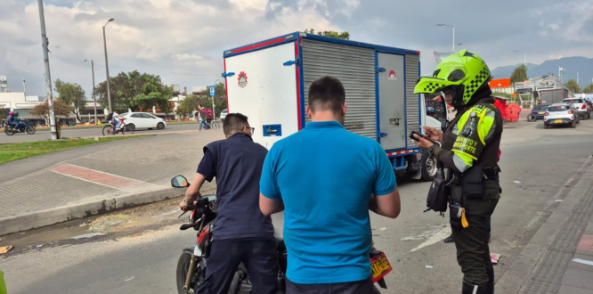 Un agente de tránsito realiza un operativo de control sobre el espacio público, verificando documentos a dos ciudadanos que se movilizaban en una motocicleta, en una vía de Puente Aranda. El procedimiento se desarrolla junto a un camión estacionado y forma parte de las acciones distritales para prevenir el parqueo indebido y recuperar el espacio público.