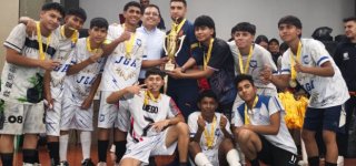 Un grupo de estudiantes celebra su victoria en los Juegos Intercolegiados 2025 de Puente Aranda. Los jóvenes, vestidos con uniformes deportivos y medallas doradas en el cuello, posan sonrientes alrededor de un gran trofeo dorado que sostienen junto a dos adultos. La escena refleja alegría, unión y logro colectivo al finalizar la competencia deportiva.