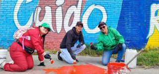“Tres personas pintan el piso de color rojo frente a un mural colorido con la palabra ‘Cuido’, como parte de una jornada comunitaria de embellecimiento en Puente Aranda.”