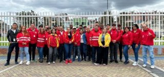 Grupo de gestores locales y funcionarios de la Alcaldía de Puente Aranda, en su mayoría con chaquetas rojas con el logo institucional, posan juntos al aire libre frente a una reja blanca, durante una jornada de capacitación para mejorar la atención integral a habitantes de calle.