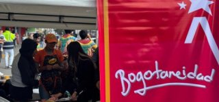 "Personas participando en una actividad comunitaria en un stand de la Alcaldía Local de Puente Aranda, con un cartel rojo que lleva el mensaje 'Bogotanidad'."