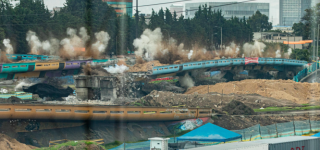 “Implosión controlada de los antiguos puentes vehiculares en la intersección de la Avenida de las Américas con la Calle 13, en Puente Aranda. La imagen muestra el momento del colapso de las estructuras, con columnas de polvo y maquinaria en operación, como parte del proceso de modernización vial de Bogotá.”